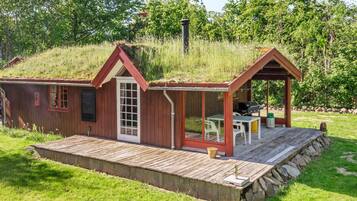 A small wooden cabin with a porch and a chimney, surrounded by grass and trees.