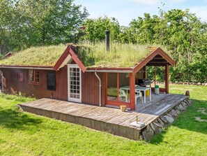 A small wooden cabin with a porch and a chimney, surrounded by grass and trees.
