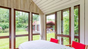 A room with a large table, chairs, and a view of a garden and a building outside.