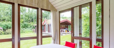 Una habitación con una mesa grande, sillas y vistas a un jardín y un edificio.