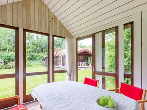A room with a large table, chairs, and a view of a garden and a building outside. - 6 Person Holiday Home in Roslev (Roslev)