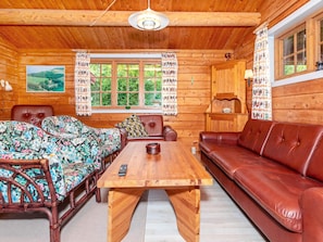 Interior d'una cabana de fusta amb una taula de fusta, dos sofàs i una finestra amb cortines.