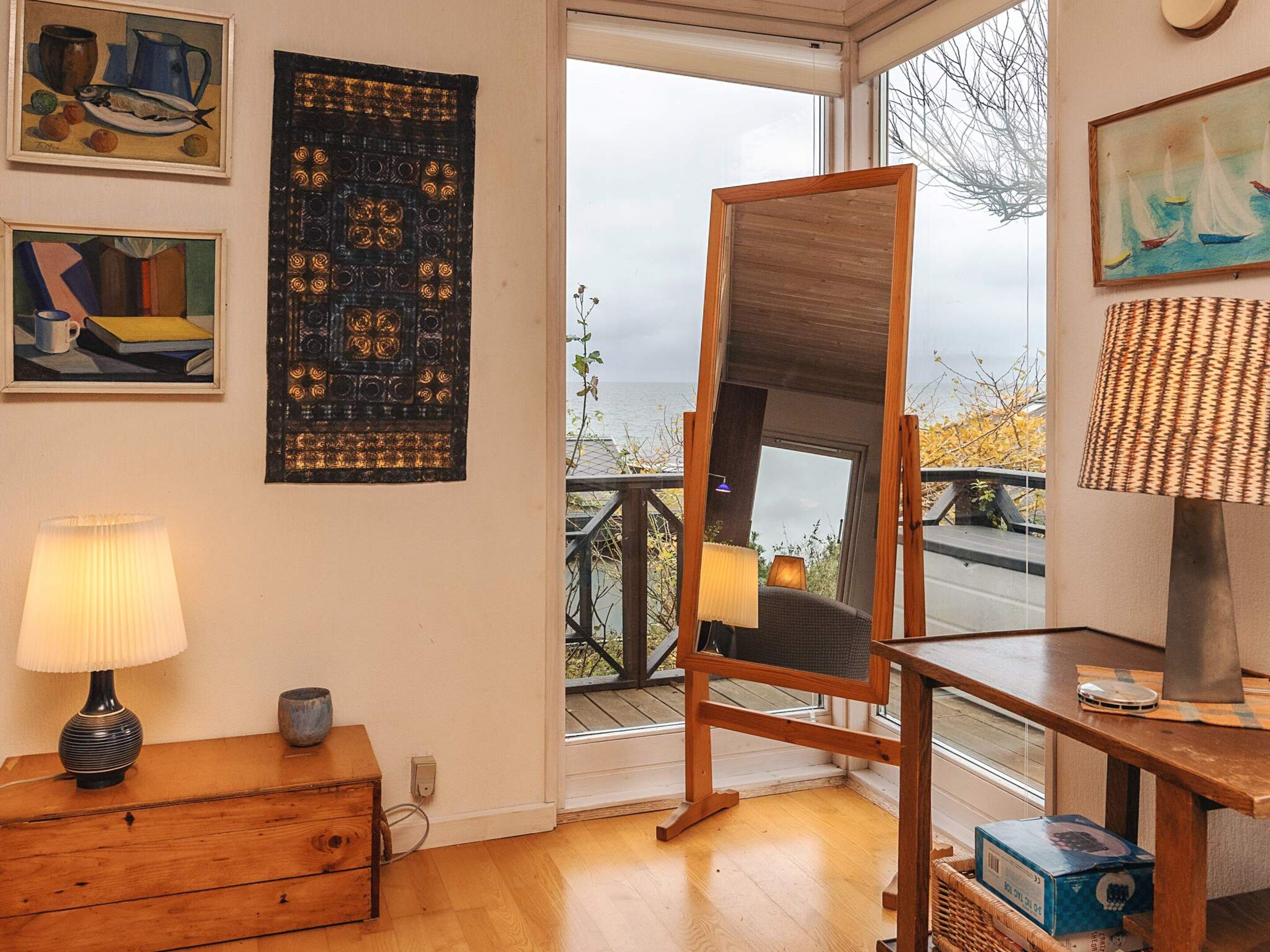 Ein Zimmer mit Holzboden, einem Stehspiegel, einer Lampe und Kunstwerken an den Wänden.
