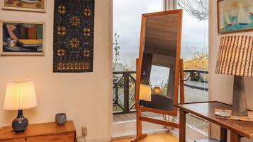 Ein Zimmer mit Holzboden, einem Stehspiegel, einer Lampe und Kunstwerken an den Wänden.
