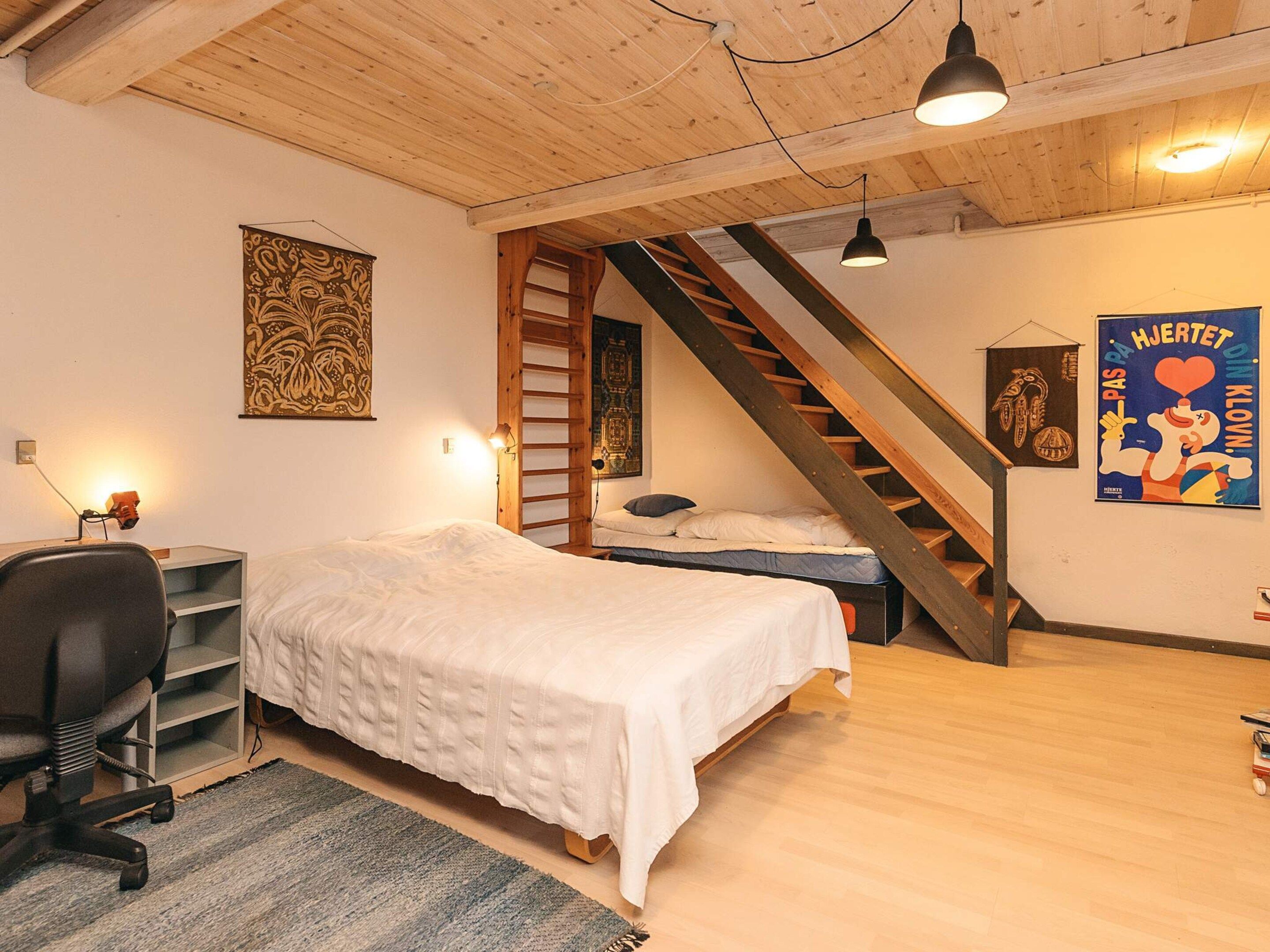 Ein Schlafzimmer mit zwei Betten, einem Schreibtisch, einem Stuhl, einer Leiter und einer Treppe.