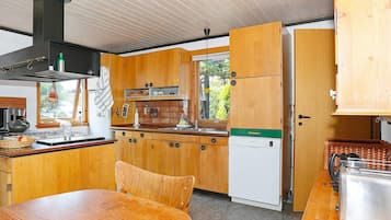 A compact kitchen with wooden cabinets, a white dishwasher, and a dining table with chairs.