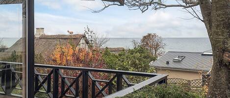 Terraza de madera con barandilla que da a la costa, con un edificio de techo de paja y vistas al mar.