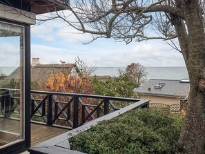 A wooden deck with a railing overlooking a coastal area, featuring a thatched-roof building and a view of the sea. - 5 Person Holiday Home in Hesselager (Hesselager)