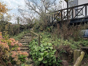 A garden with a wooden staircase surrounded by various plants and a stone wall. - 5 Person Holiday Home in Hesselager (Hesselager)