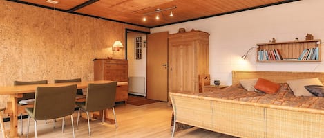 A cozy room with a wooden ceiling, a bed with patterned bedding, a dining table with chairs, and a bookshelf.