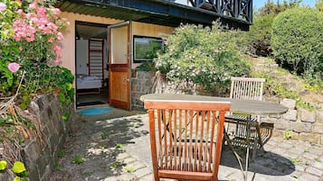 A rustic outdoor seating area with a wooden table and chairs, a stone wall, and a wooden door leading to a room.