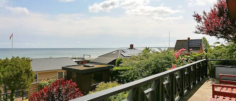 A wooden deck with a railing overlooking a residential area and a body of water.