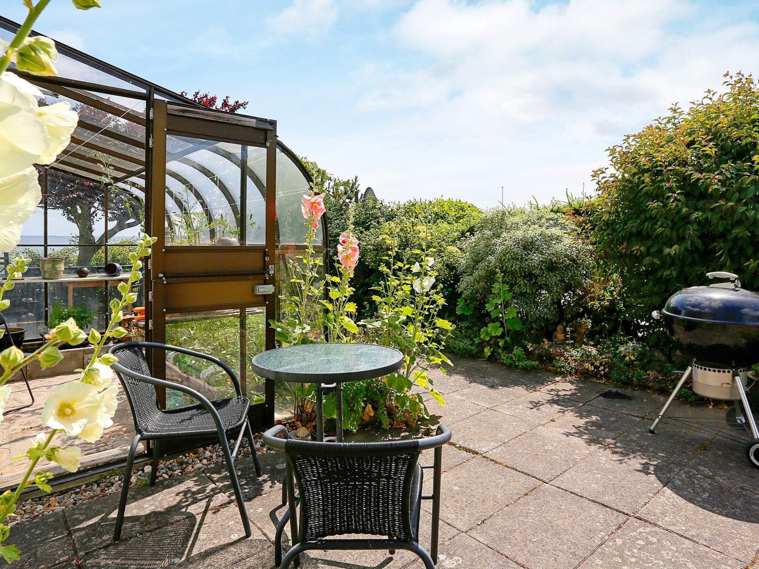 A patio with a table and chairs, a greenhouse, and a barbecue grill.