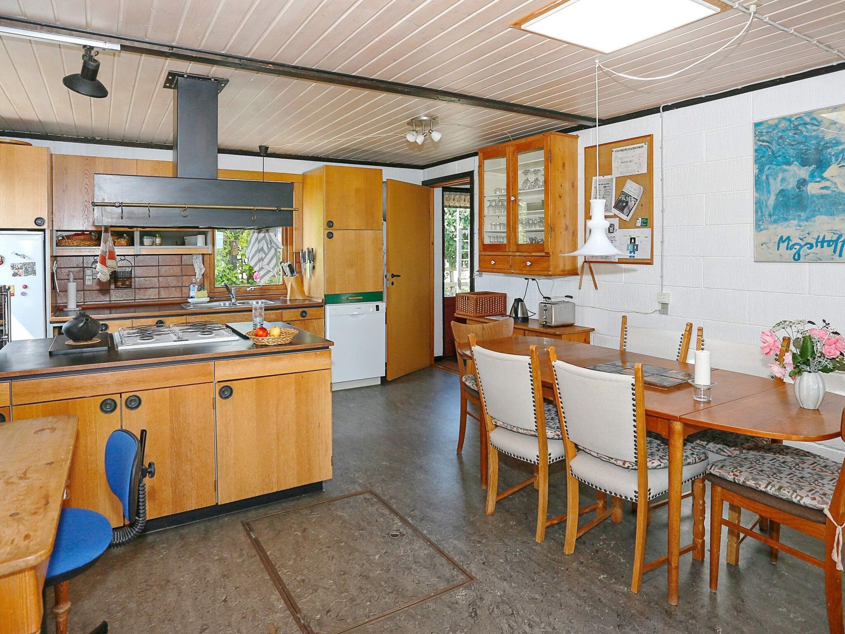 Une cuisine avec des meubles de rangement en bois, une cuisinière et un coin repas comprenant une table et des chaises.