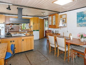 A kitchen with wooden cabinets, a stove, and a dining area with a table and chairs. - 5 Person Holiday Home in Hesselager (Hesselager)