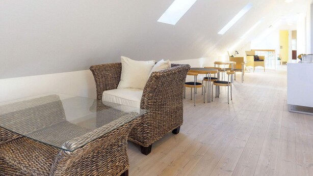 A modern loft-style living area with a glass coffee table, wicker furniture, and a dining set.