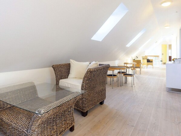 A modern loft-style living area with a glass coffee table, wicker furniture, and a dining set.