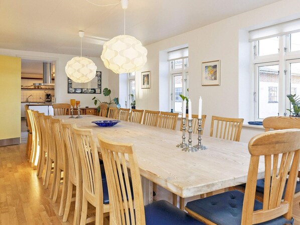 Un espace repas avec une longue table en bois, plusieurs chaises et des lampes suspendues.