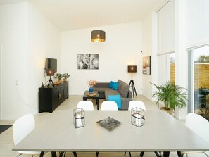 Ein modernes Wohnzimmer mit Esstisch, Sofa und Fernseher.