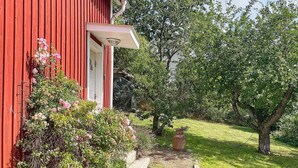 Een rood gebouw met een witte deur, omringd door groen en een stenen pad.