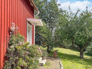 A red building with a white door, surrounded by greenery and a stone pathway. - 4 Person Holiday Home in Trensum (Trensum)