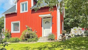 Een rode woning met een witte deur en ramen, omgeven door groen en een heldere lucht.