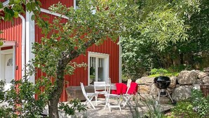 Een rode woning met een terras, buitenmeubels en een barbecue.