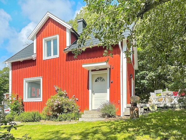 A red house with a white door and windows, surrounded by greenery and a clear sky. - 4 Person Holiday Home in Trensum (Trensum)