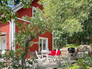 A red building with a deck area featuring outdoor furniture and a barbecue grill.