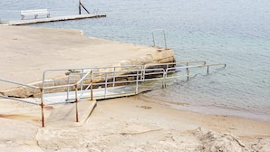 A concrete pier with a metal railing, a bench, and a rocky shoreline in the background. - 4 Person Holiday Home in Kungshamn (Kungshamn)
