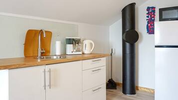Een moderne keuken met een spoelbak, koffiezetapparaat, waterkoker en een zwart, cilindervormig object, mogelijk een stofzuiger.
