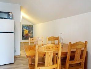 Une pièce de taille modeste, avec une table à manger en bois, quatre chaises, un réfrigérateur blanc et une affiche accrochée au mur.