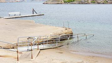A concrete dock with metal railings and a bench, leading into calm water.