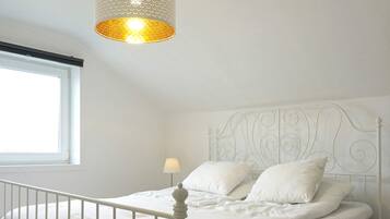 Un llit de metall blanc amb un capçal decoratiu, una barana blanca i una làmpada sobre la taula de nit.