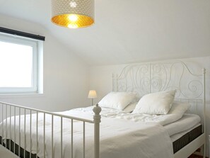 A white bed with a metal headboard, a bedside lamp, and a window with a view. - 4 Person Holiday Home in Kungshamn (Kungshamn)
