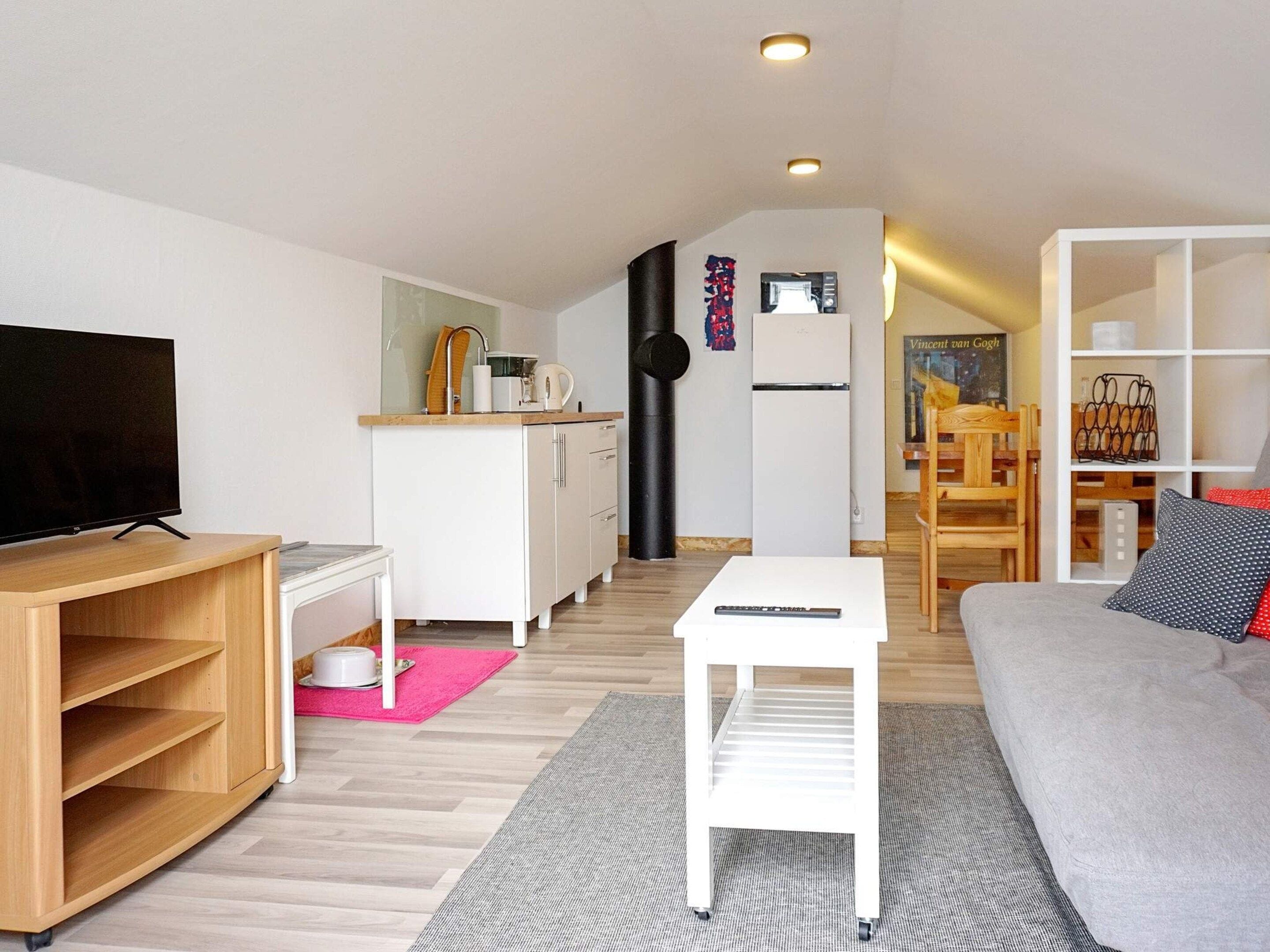 A modern living room with a flat-screen TV, a sofa, a coffee table, and a dining area with a wooden table and chairs.