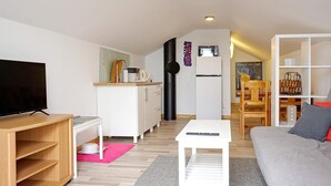 Moderni olohuone, jossa on litteänäyttöinen televisio, sohva, sohvapöytä sekä ruokailutila, jossa on puinen pöytä ja tuolit.