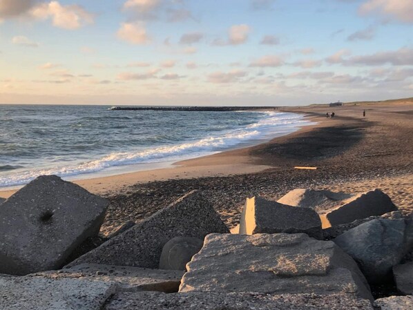 A beach with waves, a pier, and large rocks in the foreground.