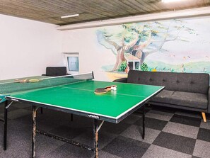Una mesa de ping pong con red, un sofá y un mural de un árbol en la pared.