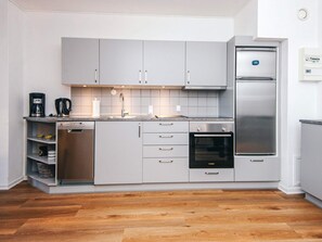 A modern kitchen with grey cabinets, a built-in oven, a stainless steel refrigerator, and a coffee maker. - 4 Person Holiday Home in Hejls (Hejls)