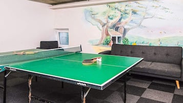 A ping pong table with a net, a sofa, and a mural of a tree on the wall.