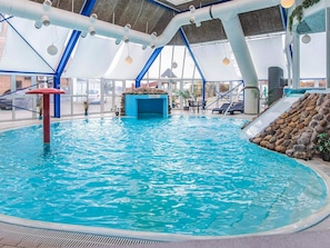 Una piscina interior amb aigua blava cristal·lina, una paret d'escalada i un tobogan.
