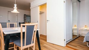 A modern dining area with a wooden table and chairs, a hanging light fixture, and a sliding door leading to another room.