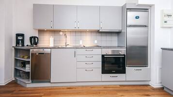 A modern kitchen with grey cabinets, a stainless steel refrigerator, a built-in oven, and a dishwasher.
