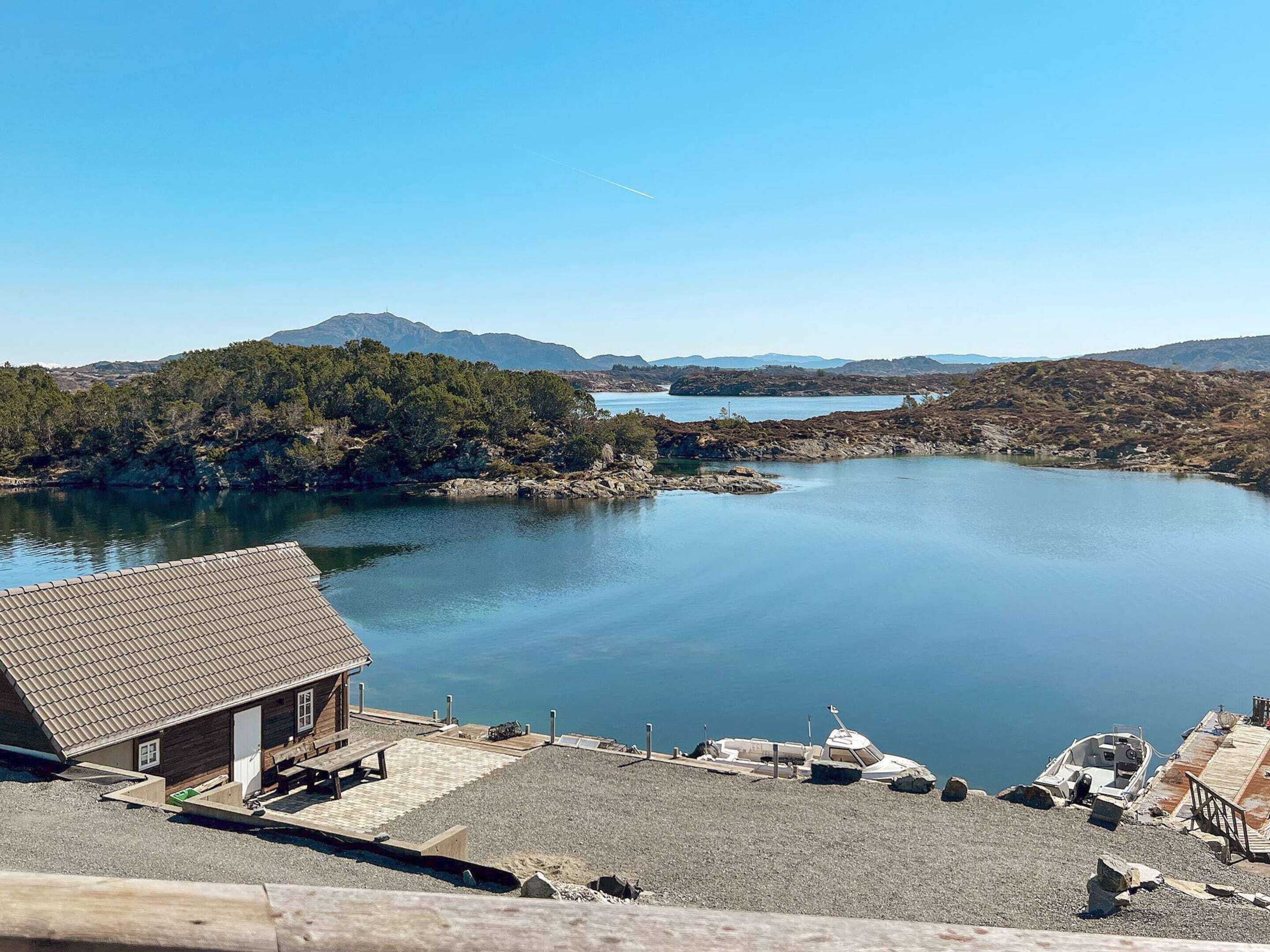 A lakeside cabin with a dock, surrounded by rocky terrain and distant mountains.