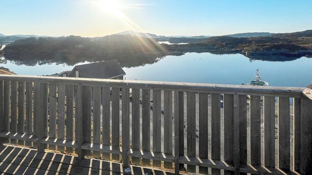 A wooden railing overlooking a calm lake with mountains in the background and a clear sky. - 6 Person Holiday Home in Bremnes (Bomlo)