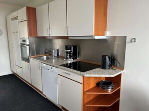 Uma cozinha compacta com armários brancos, uma pia de aço inoxidável, uma cafeteira e uma máquina de lavar louça.