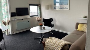 A modern hotel room with a sofa, a dining table, a TV, and a painting on the wall.