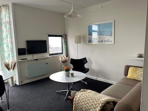 A modern hotel room with a sofa, a dining table, a TV, and a painting on the wall.