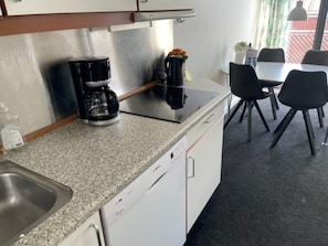 A kitchenette with a coffee maker, a sink, and a dining area with chairs and a table.